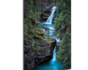 May include: A vertical print of a waterfall cascading into a turquoise pool, surrounded by lush green trees and rocky cliffs. The water flows rapidly, creating a sense of movement and tranquility. The scene captures a natural landscape.
