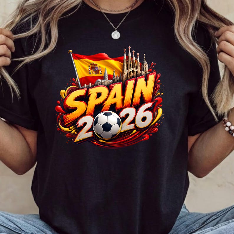 Może przedstawiać: Czarny t-shirt z nadrukiem graficznym przedstawiającym flagę Hiszpanii, Sagrada Familia oraz napis "SPAIN 2026" pogrubioną ż&oacute;łto-czerwoną czcionką. Czarno-biała piłka nożna znajduje się na środku wzoru.