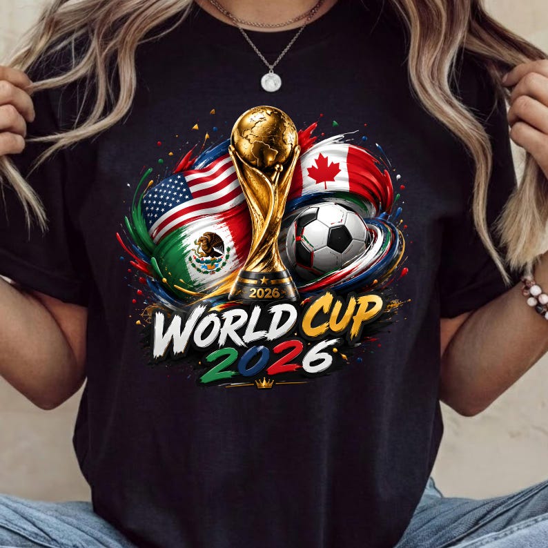Może przedstawiać: Czarny t-shirt z grafiką złotego trofeum Mistrzostw Świata 2026, piłką nożną oraz flagami Stan&oacute;w Zjednoczonych, Meksyku i Kanady. Wz&oacute;r zawiera kolorowe plamy farby oraz napis World Cup 2026 wykonany pogrubioną czcionką.
