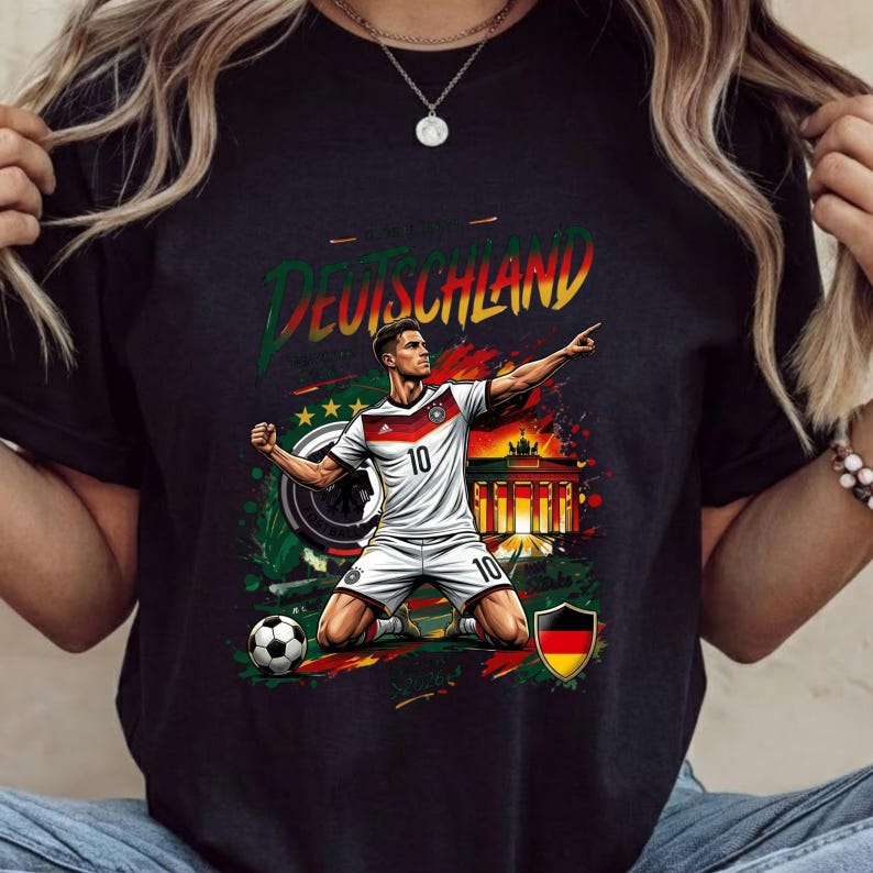 Może przedstawiać: Czarny t-shirt z grafiką piłkarza w białej koszulce z numerem 10, klęczącego na boisku. Wz&oacute;r zawiera napis DEUTSCHLAND, Bramę Brandenburską, piłkę nożną oraz niemiecką flagę umieszczoną w tarczy herbowej.