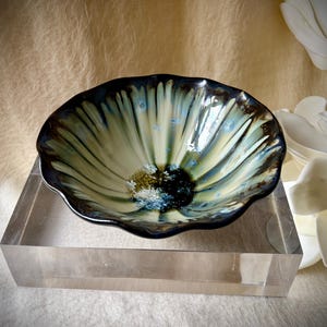 May include: A ceramic bowl with a scalloped, wavy rim featuring a crystalline glaze. The interior displays a gradient of cream and pale green radiating from a dark, deep blue centre, accented with small, star-like crystalline formations.
