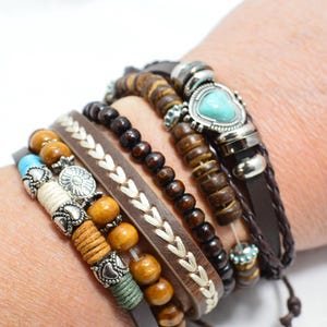 May include: A collection of stacked bracelets featuring various designs. The bracelets include wooden beads, leather straps, and turquoise accents. Some bracelets have silver-toned metal details and decorative stitching.