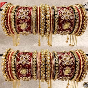 May include: A pair of ornate, red and gold bangles. The bangles feature intricate floral and geometric designs, embellished with clear and gold-toned gemstones. Delicate gold chains hang from the bangles, adding a touch of elegance. The word "NEW" is in the top left corner.