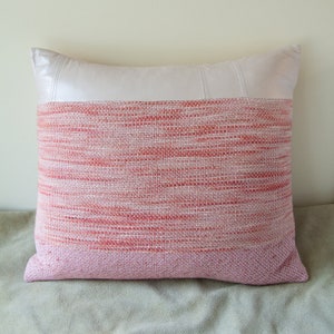May include: A pink and white striped throw pillow with a white leather accent panel. The pillow is made of a woven fabric with a subtle sheen.