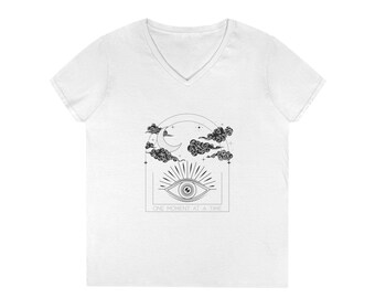 May include: White V-neck t-shirt with a black graphic design. The design features an eye with sun rays, a crescent moon, clouds, and the text "ONE MOMENT AT A TIME" in a rectangular frame. The shirt is made of a soft material.