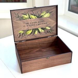 Könnte beinhalten: Geöffnete Holz-Andenkenbox mit Scharnierdeckel. Der Innendeckel zeigt ein Blumendesign mit dem Text "IN YOUR ARMS IS WHERE I BELONG". Die Box ist aus dunkelbraunem Holz und hat eine rechteckige Form. Die Box ist geöffnet und zeigt das leere Innere.