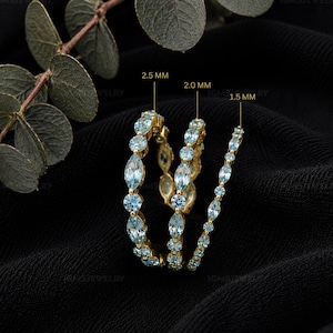 May include: Three gold rings set with light blue marquise and round cut stones. The rings are labelled with widths of 2.5 mm, 2.0 mm, and 1.5 mm, indicating the size of the stones or band width. The jewellery features a delicate, sparkling design.