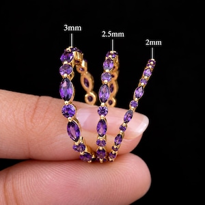 Op de afbeelding: Drie gouden ringen met afwisselend marquise en rond geslepen paarse stenen. De ringen zijn gelabeld met breedtes van 3mm, 2,5mm en 2mm, wat de grootte van de stenen aangeeft. Het ontwerp toont een doorlopende band van paarse edelstenen in goud.