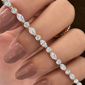 Puede incluir: Una pulsera de tenis de oro con un patrón alterno de piedras transparentes de talla marquesa y redonda. Las piedras están engastadas en una línea continua, sujetas por garras de metal dorado, creando un diseño simétrico y brillante.