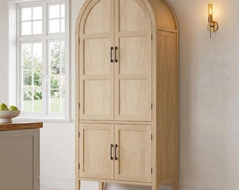 May include: A tall, light-colored wooden cabinet with an arched top. The cabinet has four doors with black handles and sits on short legs. A window and a wall sconce are visible in the background.