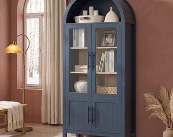 May include: A dark blue arched cabinet with two glass-paneled doors on top and two solid paneled doors on the bottom. The cabinet features black vertical handles, interior shelves holding books and decorative items, and a curved top design.
