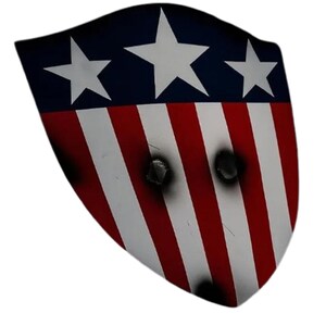 K&ouml;nnte beinhalten: Ein Schild mit patriotischem Design. Der obere Teil ist blau mit drei wei&szlig;en Sternen, der untere Teil hat rot-wei&szlig;e Streifen. Es gibt drei Einschussl&ouml;cher, die einen Used-Look erzeugen.
