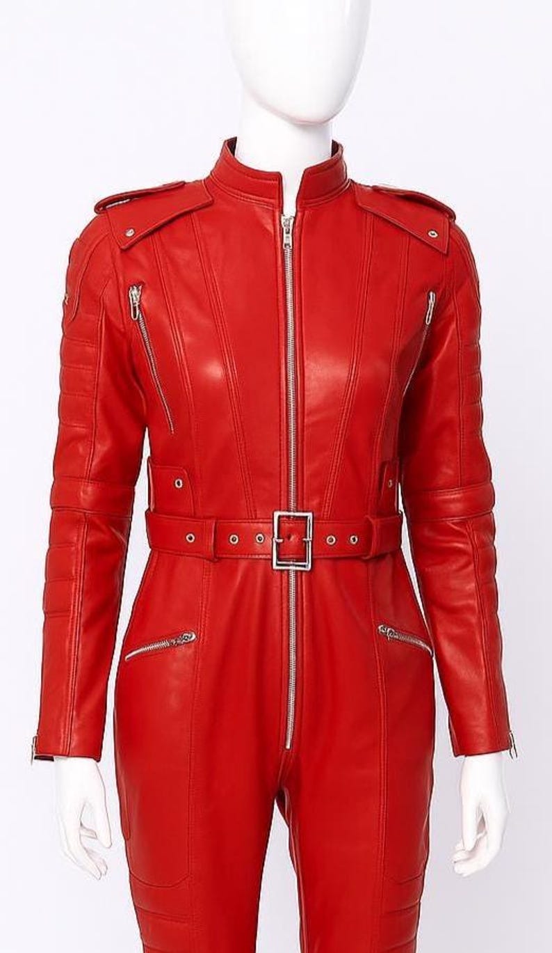 K&ouml;nnte beinhalten: Ein leuchtend roter Leder-Overall mit Stehkragen, Schulterklappen und silbernem Rei&szlig;verschluss. Der Overall hat eine Taille mit G&uuml;rtel und quadratischer Schnalle sowie mehrere Rei&szlig;verschlusstaschen. Das Kleidungsst&uuml;ck wird auf einer Schaufensterpuppe pr&auml;sentiert.
