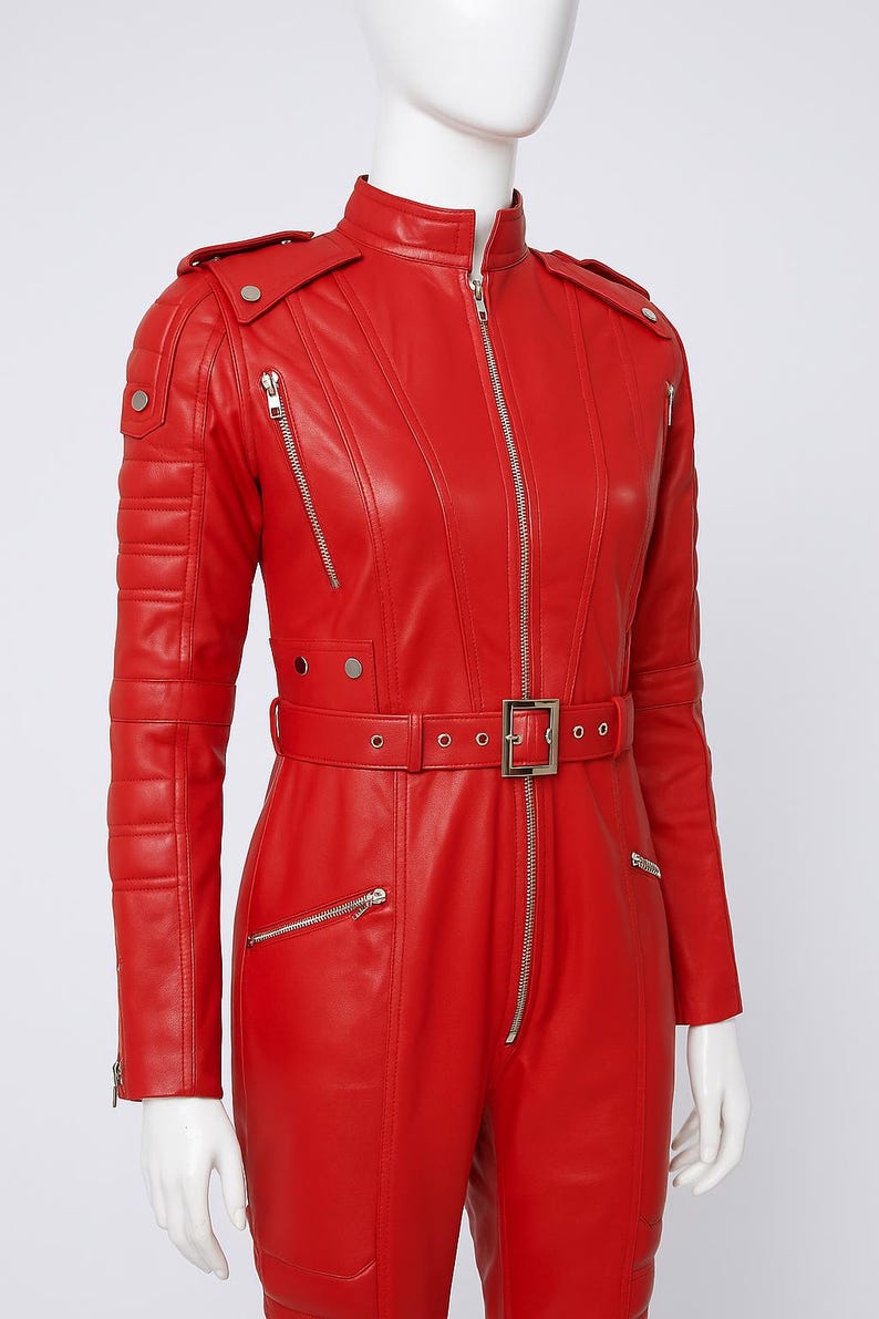 K&ouml;nnte beinhalten: Ein leuchtend roter Leder-Overall mit Stehkragen und Frontrei&szlig;verschluss. Der Overall hat einen G&uuml;rtel in der Taille, mehrere Rei&szlig;verschlusstaschen und Steppdetails an Schultern und &Auml;rmeln. Das Design ist schlicht und modern.