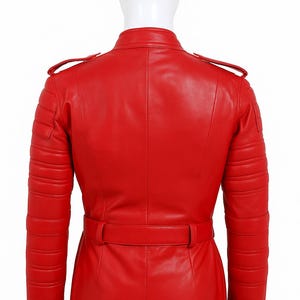 K&ouml;nnte beinhalten: Eine leuchtend rote Lederjacke mit einem Tailleng&uuml;rtel und gesteppten Details an Schultern und Armen. Die Jacke hat einen Stehkragen und Schulterklappen. Die R&uuml;ckansicht zeigt den ma&szlig;geschneiderten Schnitt und das Design des Kleidungsst&uuml;cks.