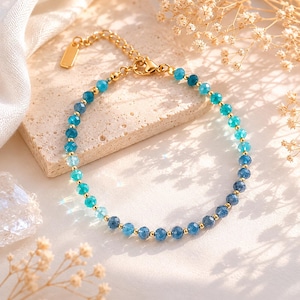 Könnte beinhalten: Armband mit einer Abstufung aus blauen und türkisfarbenen Edelsteinen. Das Armband hat einen goldenen Kettenverschluss und ein kleines goldenes Etikett. Die Edelsteine gehen von dunkelblau zu hellblau über. Die Länge beträgt ca. 18 cm.