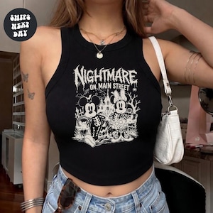 A woman wearing a black crop top with a graphic design featuring Minnie Mouse and a spooky nighttime scene.