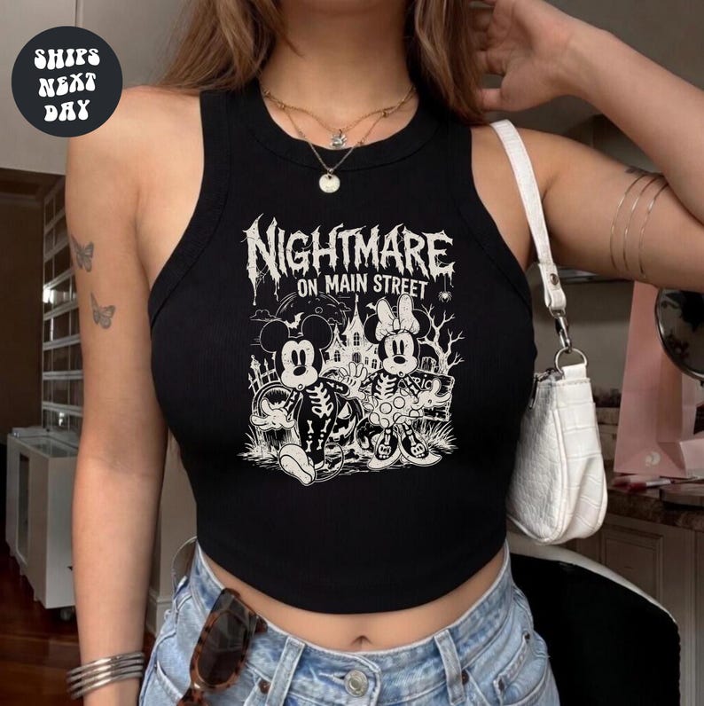 A woman wearing a black crop top with a graphic design featuring Minnie Mouse and a spooky nighttime scene.