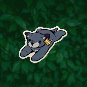 May include: A sticker featuring a cartoon-style gray cat in a pouncing position. The cat has dark gray ears, a light gray muzzle, and a white chest patch. A small orange tag with a white lightning bolt symbol is attached to the cat's ear.