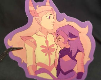May include: A sticker featuring two cartoon characters in a purple and pink color scheme. One character has long, flowing blonde hair and a light yellow outfit with a pink floral design. The other character has short purple hair and a dark purple outfit.
