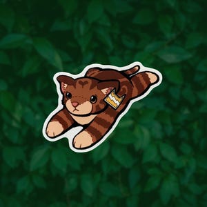 May include: A brown and tan tabby cat sticker with dark brown stripes, a heart-shaped marking on its forehead, and a small yellow tag featuring a white lightning bolt symbol attached to its ear, depicted in a playful, outstretched pose.