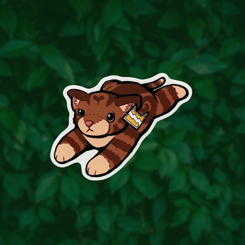 May include: A brown and tan tabby cat sticker with dark brown stripes, a heart-shaped marking on its forehead, and a small yellow tag featuring a white lightning bolt symbol attached to its ear, depicted in a playful, outstretched pose.