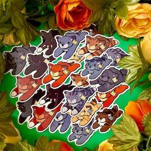 May include: A collection of die-cut stickers featuring cartoon cats in various colors including orange, grey, brown, and black. Each cat is depicted in a pouncing pose with a small, rectangular tag attached to its ear, showcasing diverse feline patterns.