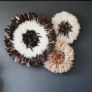 Peut inclure: Trois décorations murales en plumes. La plus grande est circulaire, avec un centre blanc et un anneau de plumes marron et noires. Deux décorations rondes plus petites sont également visibles, une blanche et une beige, sur fond gris.