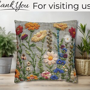 Pu&ograve; includere: Cuscino decorativo grigio ricamato con fiori colorati, tra cui fiori arancioni, gialli, rossi e blu. Il testo "Thank You For visiting us" &egrave; in alto. Il cuscino &egrave; posto davanti a un muro di colore chiaro.