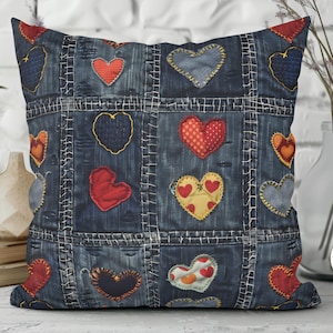 May include: Square denim pillow with a patchwork design featuring various heart shapes in red, yellow, and blue. The pillow has a quilted appearance with visible stitching, creating a rustic, handcrafted aesthetic. The pillow is a decorative home good.