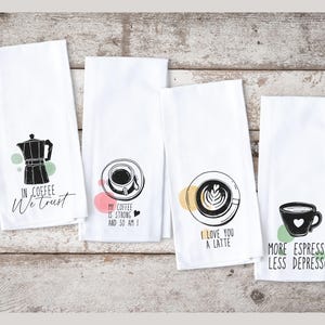 Może przedstawiać: Cztery białe ręczniki kuchenne z czarnymi wzorami o tematyce kawowej. Jeden ręcznik ma grafikę z kawiarką i napis "IN COFFEE We trust". Inne ręczniki przedstawiają grafiki filiżanek do kawy z napisami.