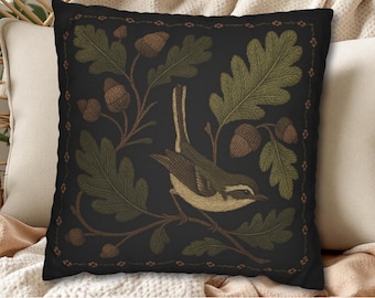 May include: A square throw pillow with a black background featuring an embroidered design of a small bird perched on an oak branch. The branch includes green oak leaves and brown acorns. A thin decorative border frames the central illustration.