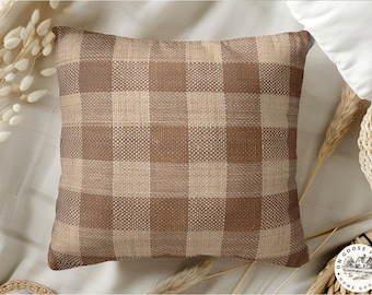 May include: Square decorative pillow with a brown and tan plaid pattern. The pillow has a woven texture and is placed on a neutral-colored surface. The pillow is a home decor item.