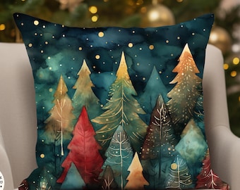 May include: A square throw pillow featuring a watercolor-style forest scene with stylized evergreen trees in shades of deep teal, forest green, red, and gold. The dark background is accented with scattered gold dots resembling falling snow.