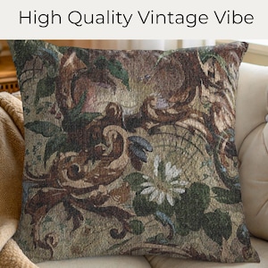 May include: Square decorative pillow with a vintage floral pattern in shades of brown, green, and cream. The pillow has a textured appearance and is placed on a beige sofa. The text "High Quality Vintage Vibe" is at the top.