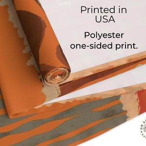 Op de afbeelding: Een polyester tafelloper met een abstract patroon van roestoranje, cr&egrave;me en grijze strepen. De tekst Printed in USA en Polyester one-sided print is zichtbaar op de witte onderkant. Een rond logo toont de tekst On Goose Pond Home Goods.
