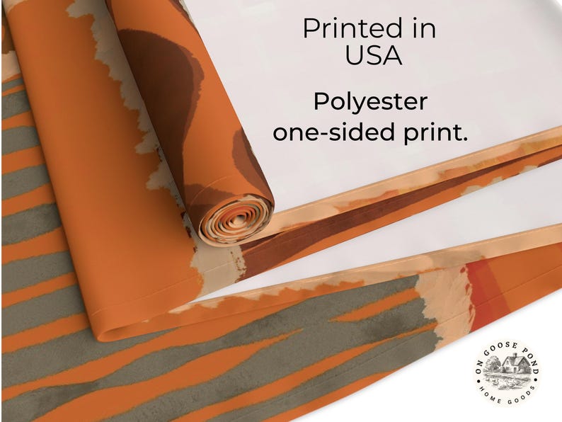 Op de afbeelding: Een polyester tafelloper met een abstract patroon van roestoranje, cr&egrave;me en grijze strepen. De tekst Printed in USA en Polyester one-sided print is zichtbaar op de witte onderkant. Een rond logo toont de tekst On Goose Pond Home Goods.