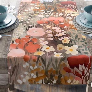 May include: A table runner featuring a watercolor-style floral pattern in shades of terracotta, burnt orange, cream, and muted green. The design includes various stylized flowers and foliage. A circular logo in the corner reads On Goose Pond Home Goods.