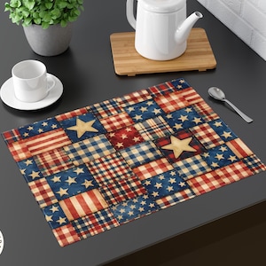 May include: A rectangular placemat with a patchwork design featuring the American flag, stars, and plaid patterns in red, white, and blue. A white teacup and saucer, a teapot, and a spoon are on the dark surface.
