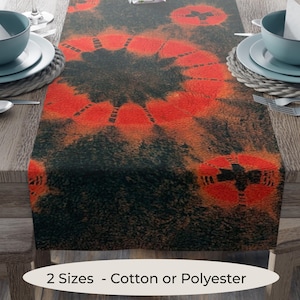 May include: A decorative table runner with a dark background and vibrant red circular patterns. The runner is made of cotton or polyester and is displayed on a wooden table. The text "2 Sizes - Cotton or Polyester" is visible.