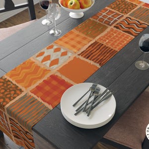 Op de afbeelding: Een rechthoekige tafelloper met een patchworkontwerp van diverse herfstachtige patronen in tinten oranje, bruin en cr&egrave;me. De stoffen vierkanten tonen motieven zoals ruiten, strepen, golvende lijnen en argyle, wat zorgt voor een gestructureerd uiterlijk.