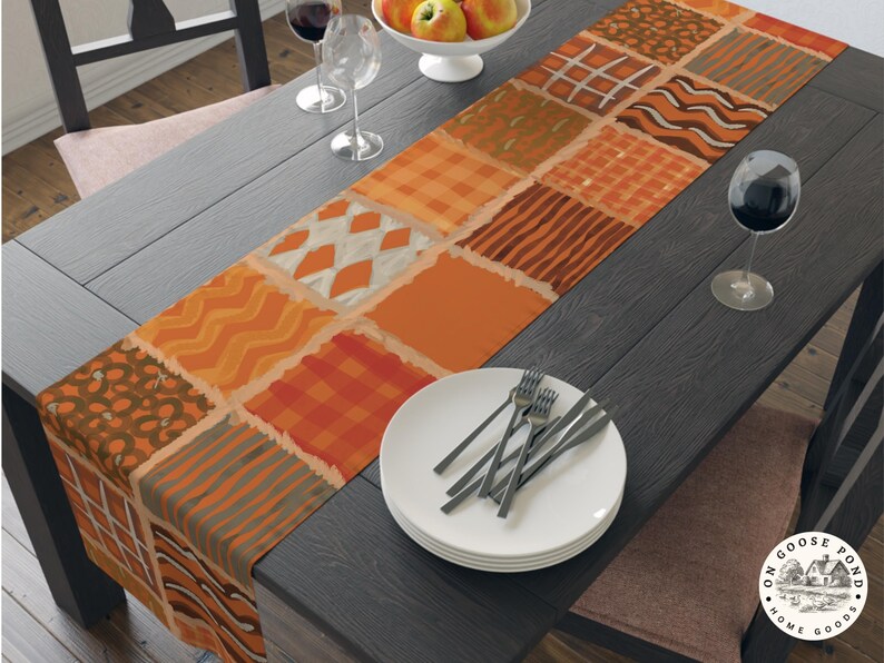Op de afbeelding: Een rechthoekige tafelloper met een patchworkontwerp van diverse herfstachtige patronen in tinten oranje, bruin en cr&egrave;me. De stoffen vierkanten tonen motieven zoals ruiten, strepen, golvende lijnen en argyle, wat zorgt voor een gestructureerd uiterlijk.
