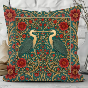 May include: Decorative square pillow with a teal background and a floral and bird design. The pillow features two herons facing each other, surrounded by red flowers and gold accents. The pillow is a square shape.