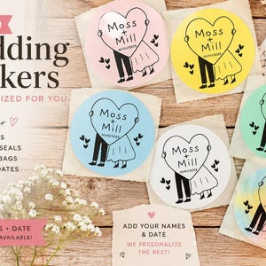 May include: A collection of circular stickers featuring a black line drawing of two figures holding a heart with the text Moss + Mill and 10/21/2025. The stickers come in pink, yellow, blue, white, green, and a multi-colored watercolor finish.
