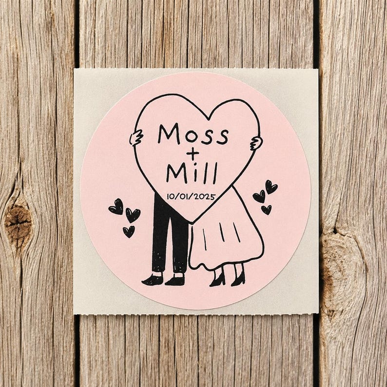 May include: A circular light pink sticker featuring a black line drawing of two figures standing behind a large heart. The heart contains the text Moss + Mill and the date 10/01/2025. Several small black hearts are scattered around the figures.