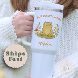 May include: White tumbler with a handle featuring a cartoon frog on a lily pad, with the text "NOT TODAY CHAOS" and the name "Madison" in orange. The tumbler has a silver rim and a white lid.