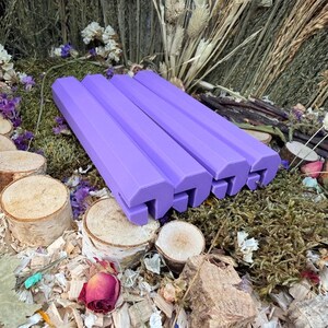 May include: Four elongated, lavender-coloured, hexagonal-shaped bars with a notched slot running along the bottom edge. These solid, smooth-surfaced objects are arranged in a parallel row, showcasing a uniform matte finish and geometric design.