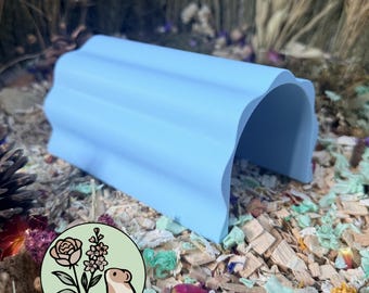 May include: A light blue, arched tunnel hideout for small pets with a corrugated, wavy exterior surface. The structure is open on both ends and features a smooth, matte finish, providing a simple, functional shelter for small animals.