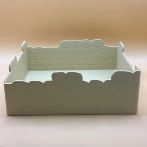 May include: An off-white rectangular tray with a stone-effect pattern. The tray has a scalloped edge and a smooth interior. The design mimics a miniature stone wall, suitable for decorative purposes.