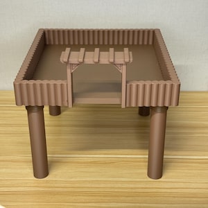 May include: A brown, miniature table with a rectangular top and four cylindrical legs. The table has a decorative border and a small archway structure on one side. The table is likely a toy or decorative item.